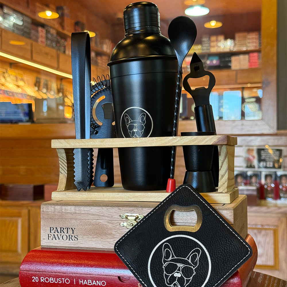 Black cocktail shaker set with a dog logo, arranged on a wooden stand, surrounded by bar tools in a cozy bar setting.