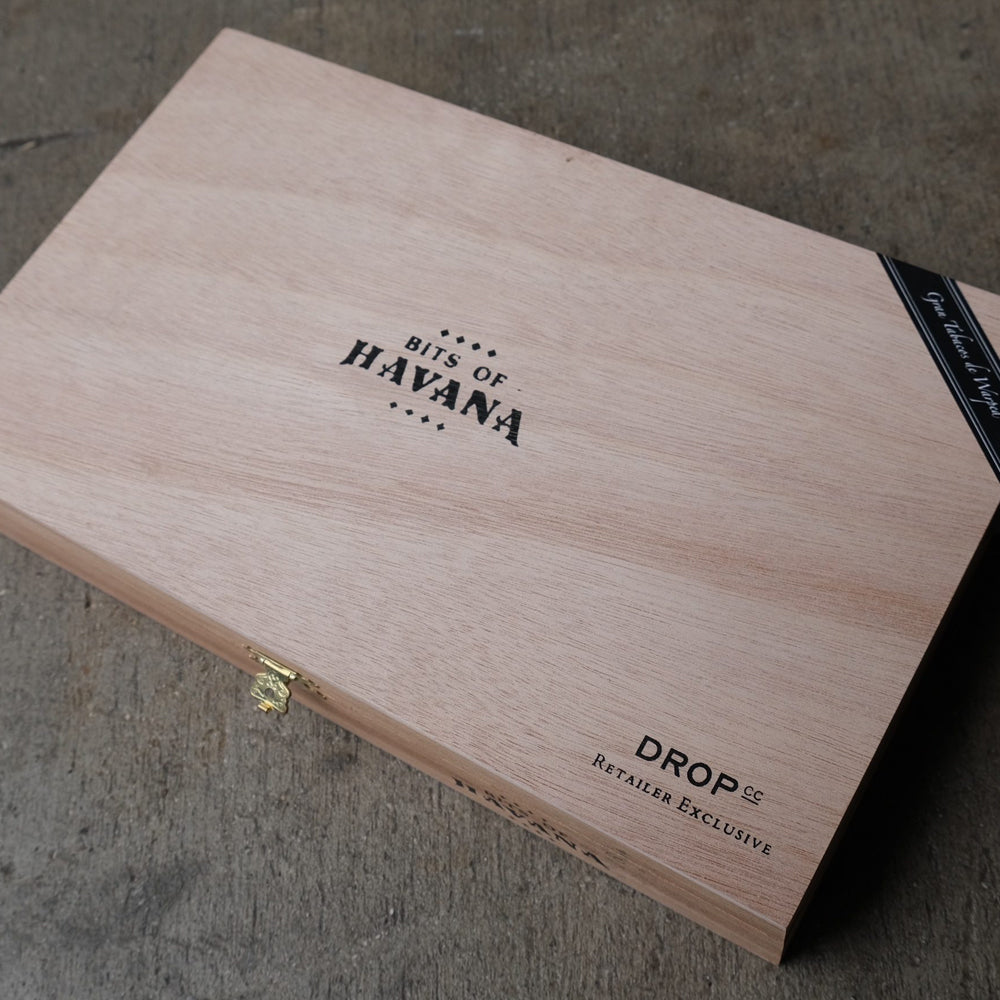 Wooden box labeled "Bits of Havana" with a gold latch, positioned on a textured surface.